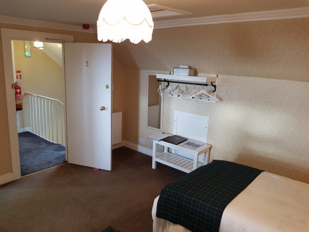 Une chambre à coucher comprenant un lit, une petite table, un porte-manteau et une porte donnant sur un escalier.