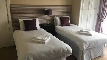 A hotel room with two single beds, a nightstand with a lamp, and a door with a curtain.