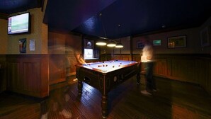 A pool table in a dimly lit room with wooden flooring and a television mounted on the wall. - The Station Hotel (Carnoustie)