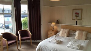 A hotel room with a bed, a chair, a nightstand, and a window with curtains. - The Station Hotel (Carnoustie)