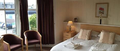 Una habitación de hotel con cama, una silla, una mesita de noche y una ventana con cortinas.