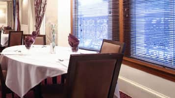 A dining area with round tables, chairs, and a window with blinds.