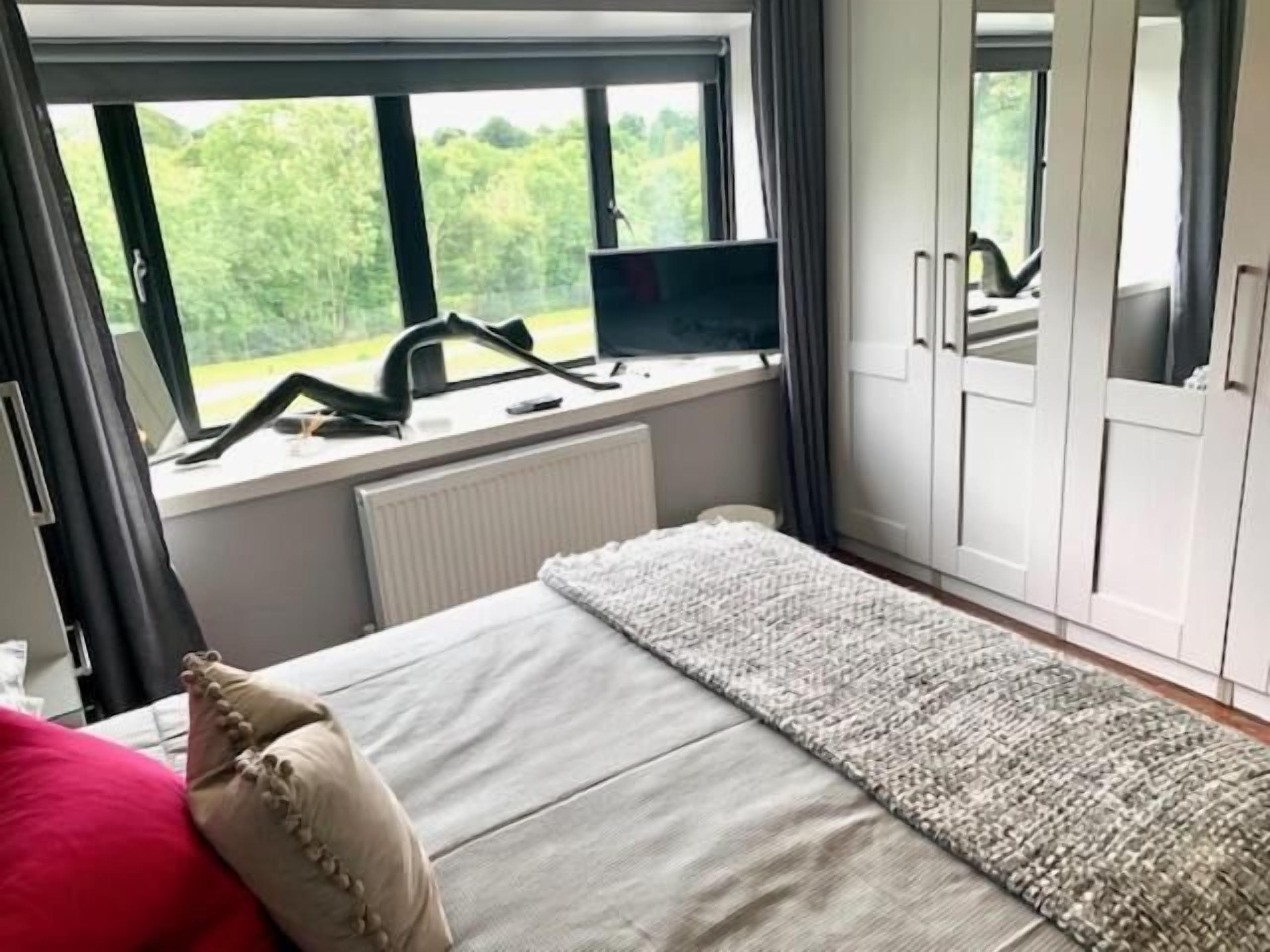 Une chambre avec une grande fenêtre, un lit avec des oreillers, un radiateur et une armoire.