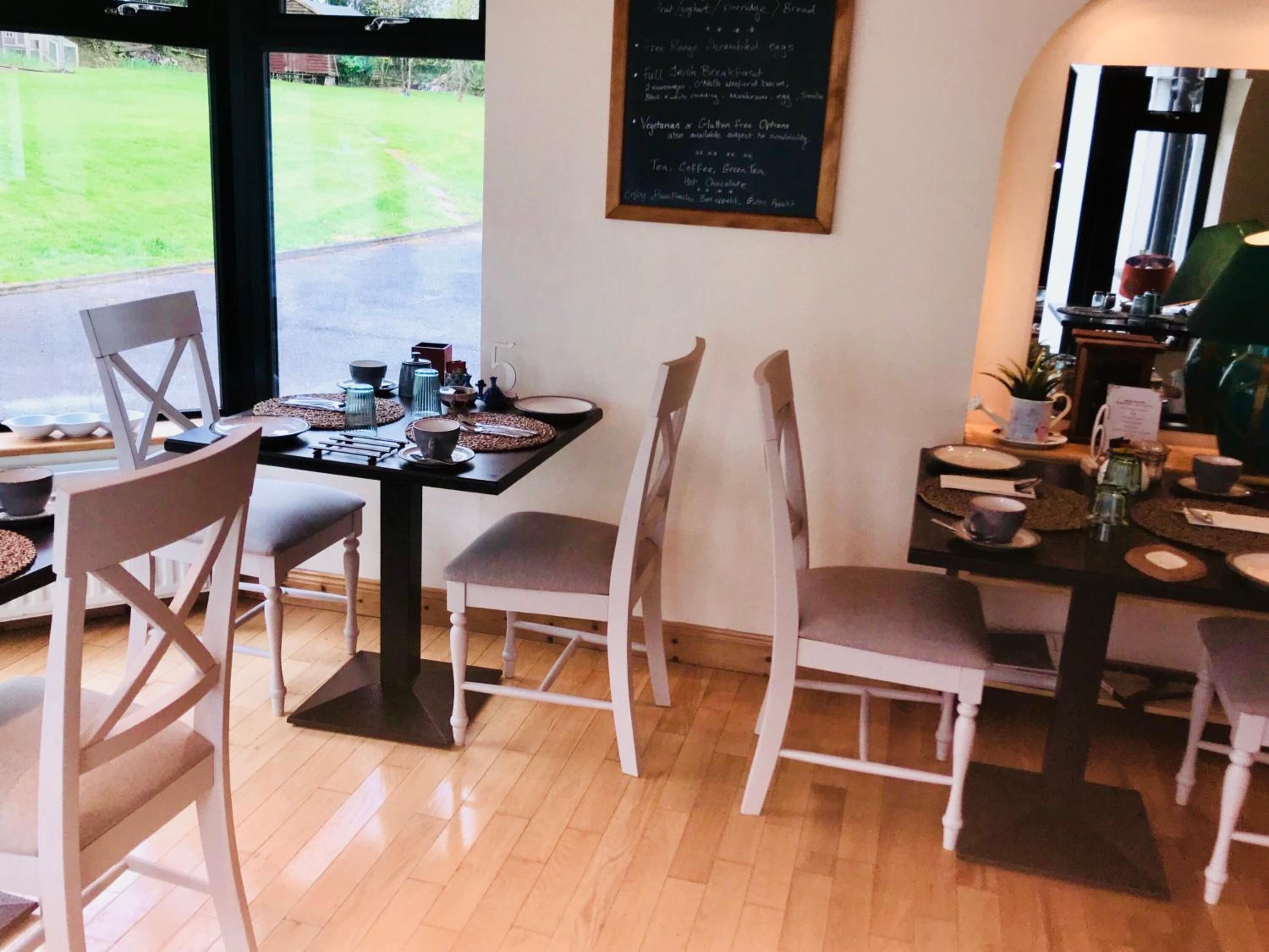 Un comedor con una mesa preparada para cuatro, sillas, un menú en una pizarra y vistas a un área verde exterior.
