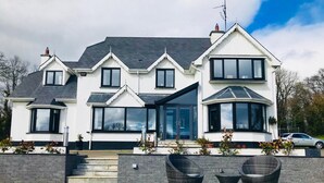 A two-story house with a large front porch, a covered patio, and a car parked in the driveway. - Railway Country House B&B (Gorey)