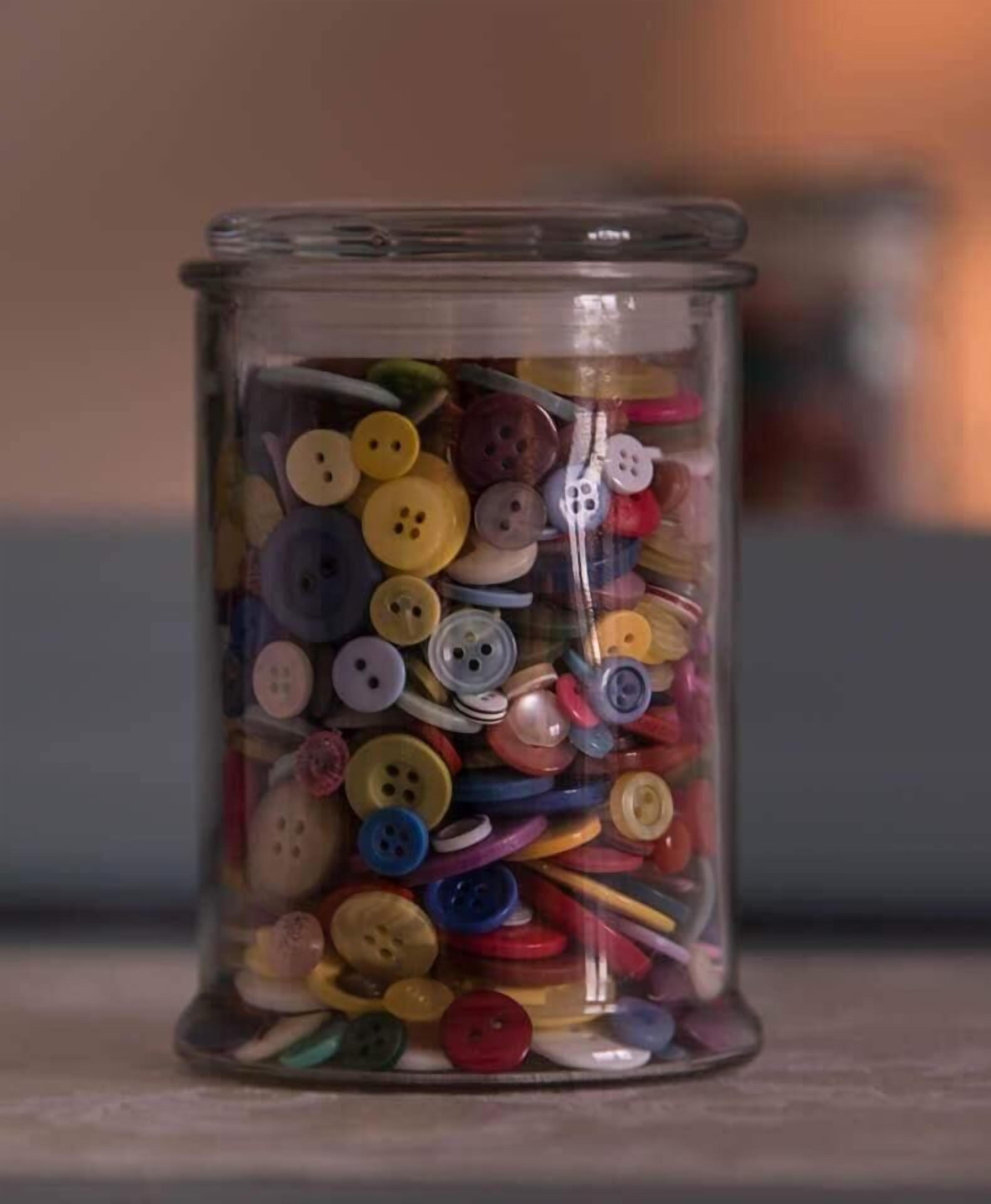A clear glass jar filled with various colorful buttons.