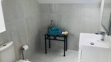 A small bathroom with a toilet, sink, and a small table with a towel and a decorative item.