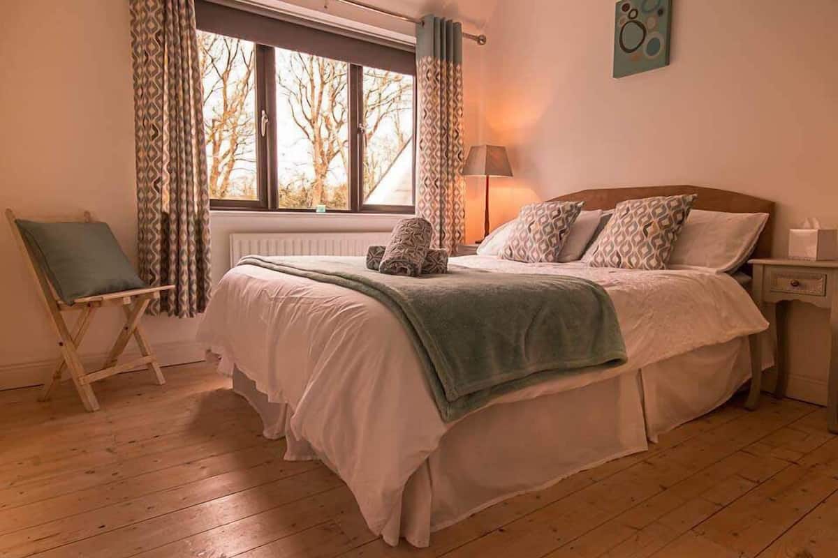 A bedroom with a bed, a chair, a lamp, and a window with curtains.