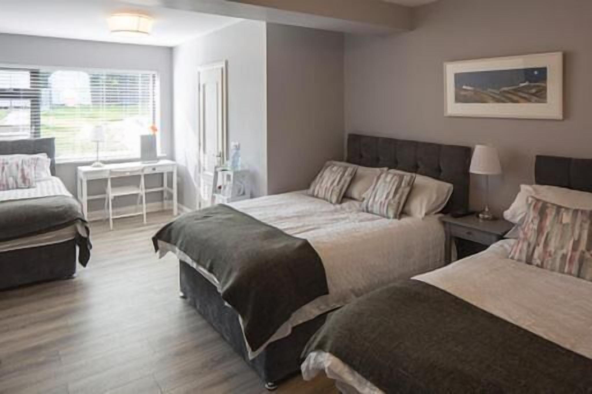 A bedroom with two beds, a bedside table, a lamp, and a window with blinds.