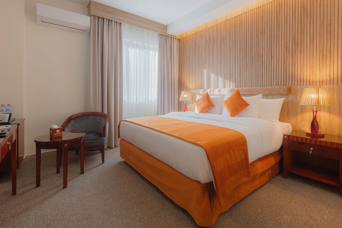 A hotel room with a large bed, a desk, a chair, and a nightstand with lamps.