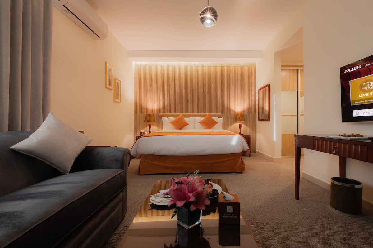 A hotel room with a bed, a sofa, a TV, and a coffee table with a flower vase.