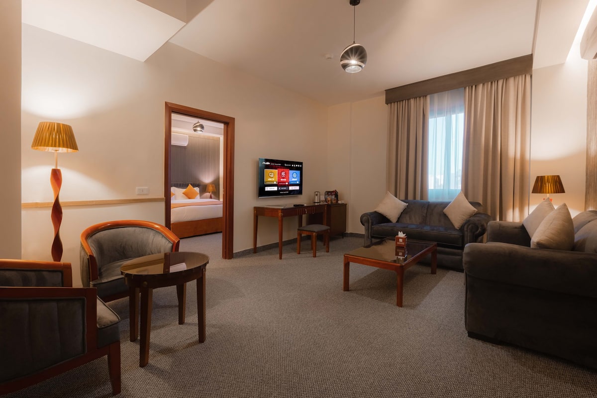A hotel room with a sofa, armchairs, a coffee table, a TV, and a desk.