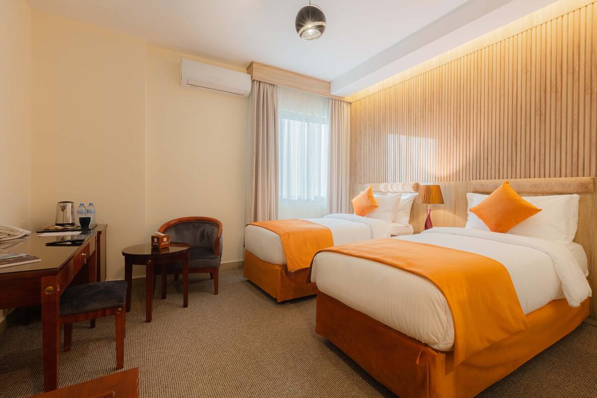 A hotel room with two beds, a desk, a chair, and a small table.