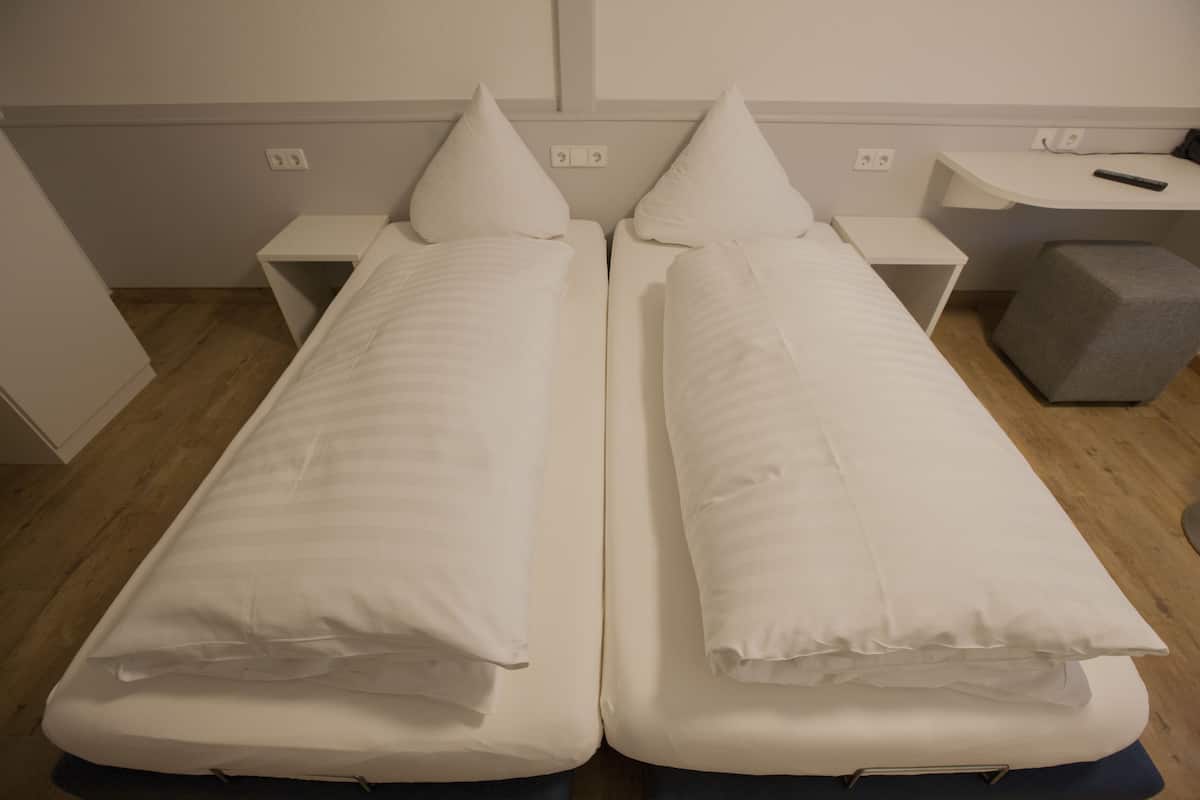 Een kamer met twee eenpersoonsbedden, elk met een kussen en een nachtkastje.
