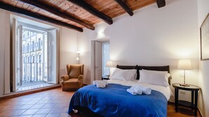 A hotel room with a large bed, a chair, a nightstand, and a view of the outside. - Palazzo Marigliano (Naples)