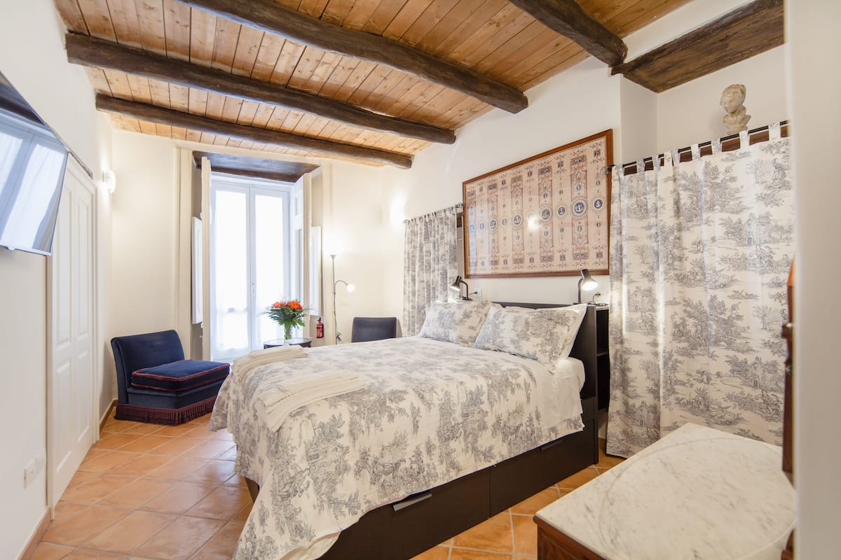 A bedroom with a large bed, a wooden ceiling, a window, and a door.