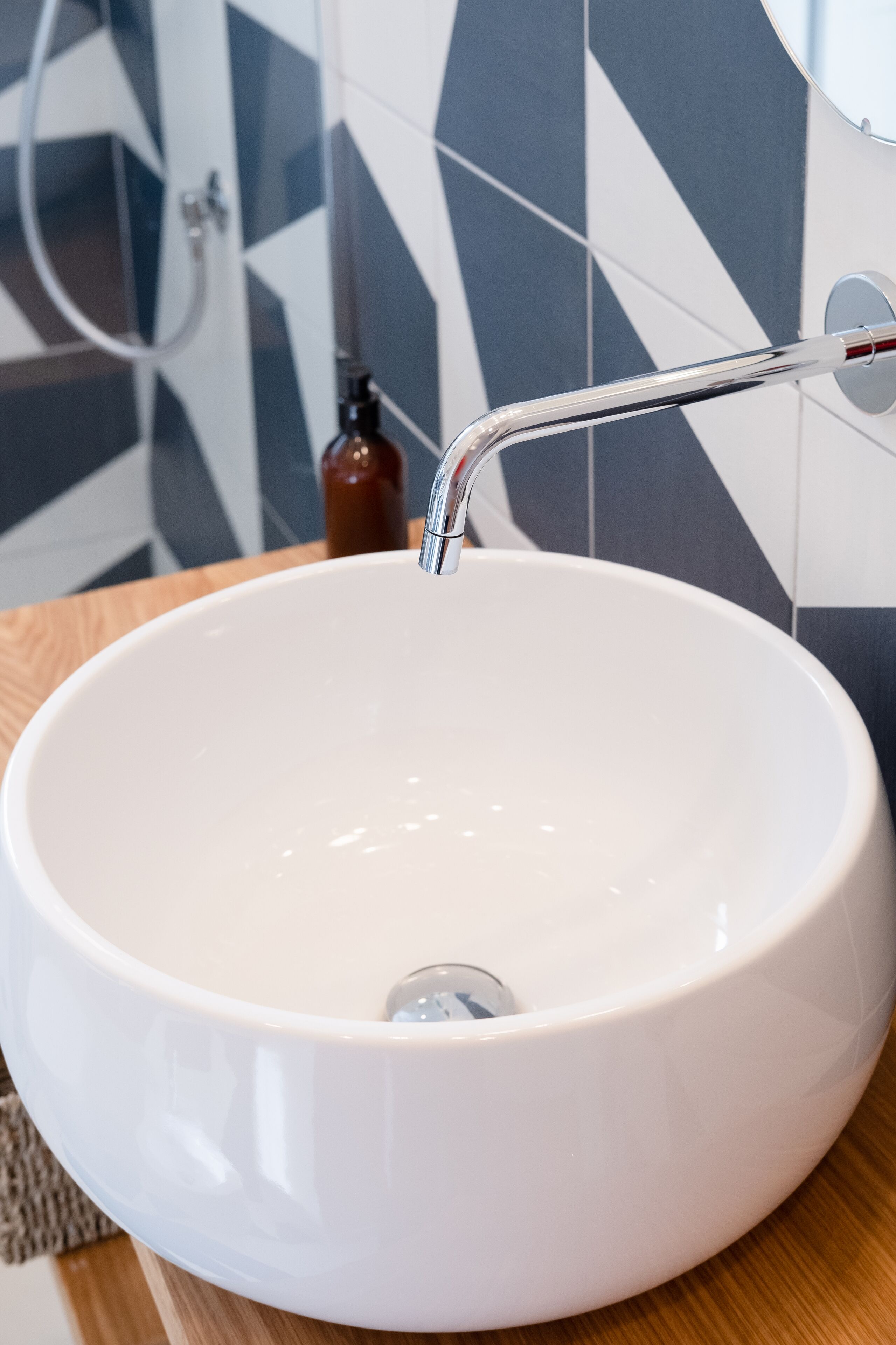 A white ceramic sink with a chrome faucet in a bathroom with geometric patterned tiles.