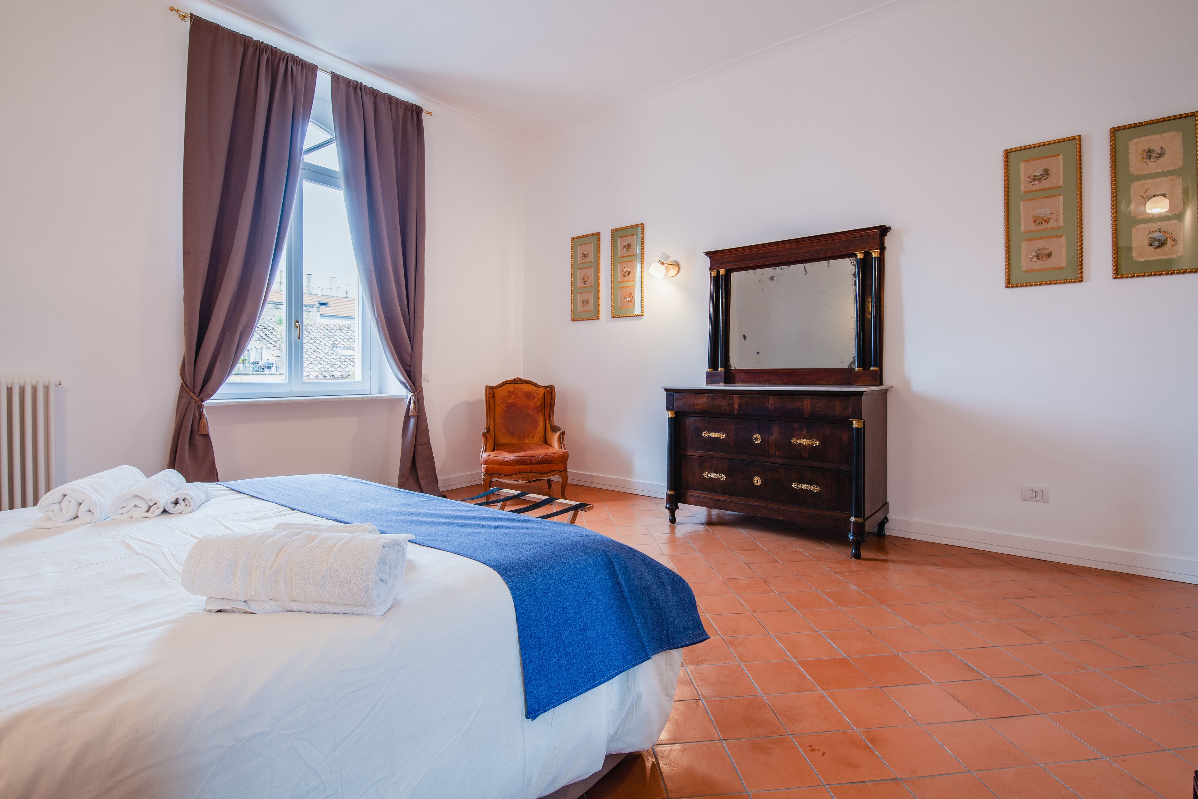 A hotel room with a bed, a dresser, a chair, and a window with curtains.