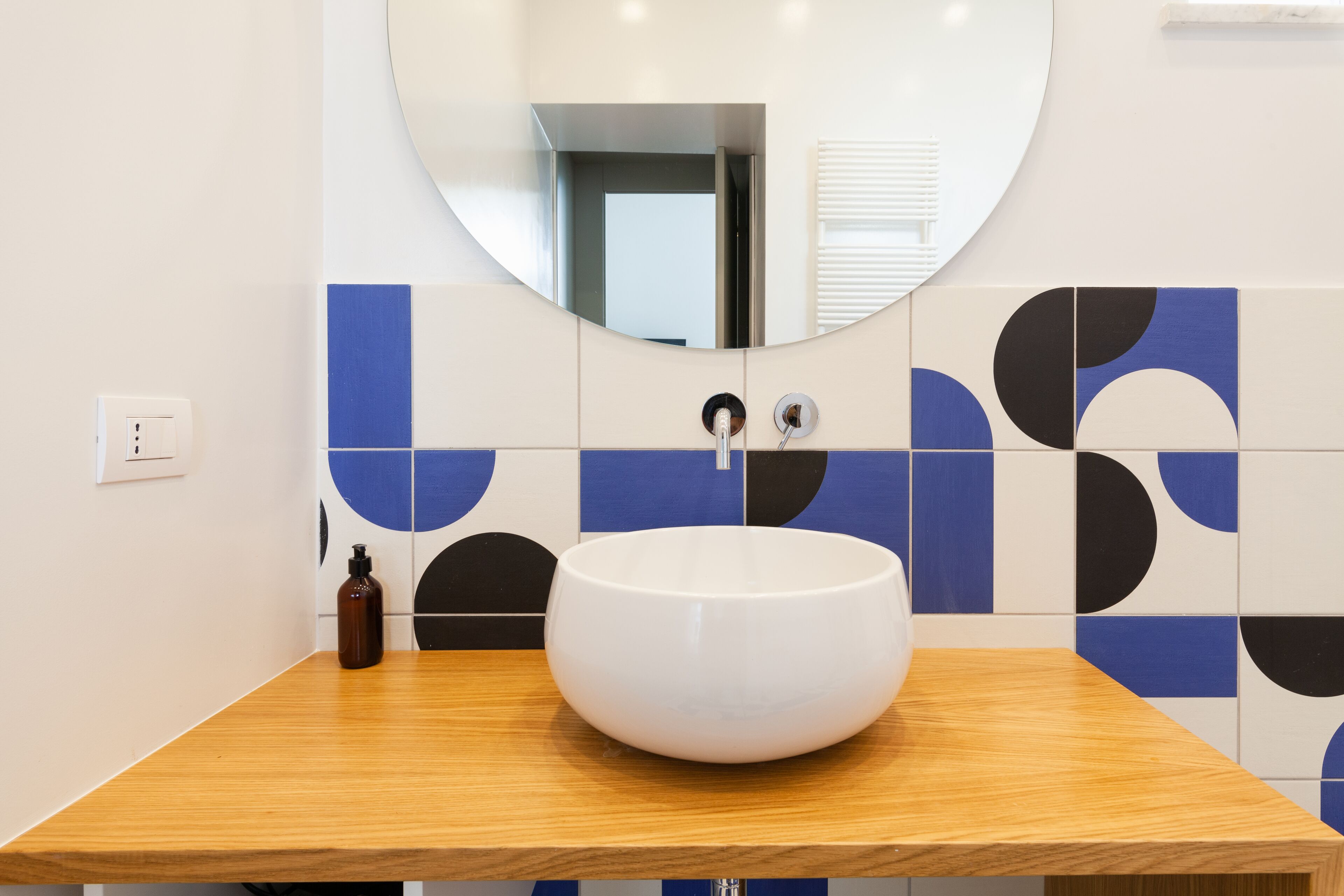 Un baño con un espejo redondo, un lavamanos blanco y azulejos con diseño azul y negro.