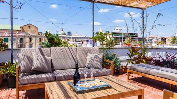 A rooftop terrace with a sofa, a wooden table, and potted plants. - Palazzo Marigliano (Naples)
