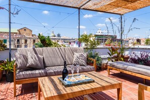 A rooftop terrace with a sofa, a wooden table, and potted plants. - Palazzo Marigliano (Naples)