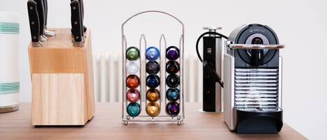 A wooden knife block with knives, a colorful spray bottle holder, and a coffee machine on a wooden table.