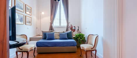 A bedroom with a bed, two chairs, a TV, and a radiator.