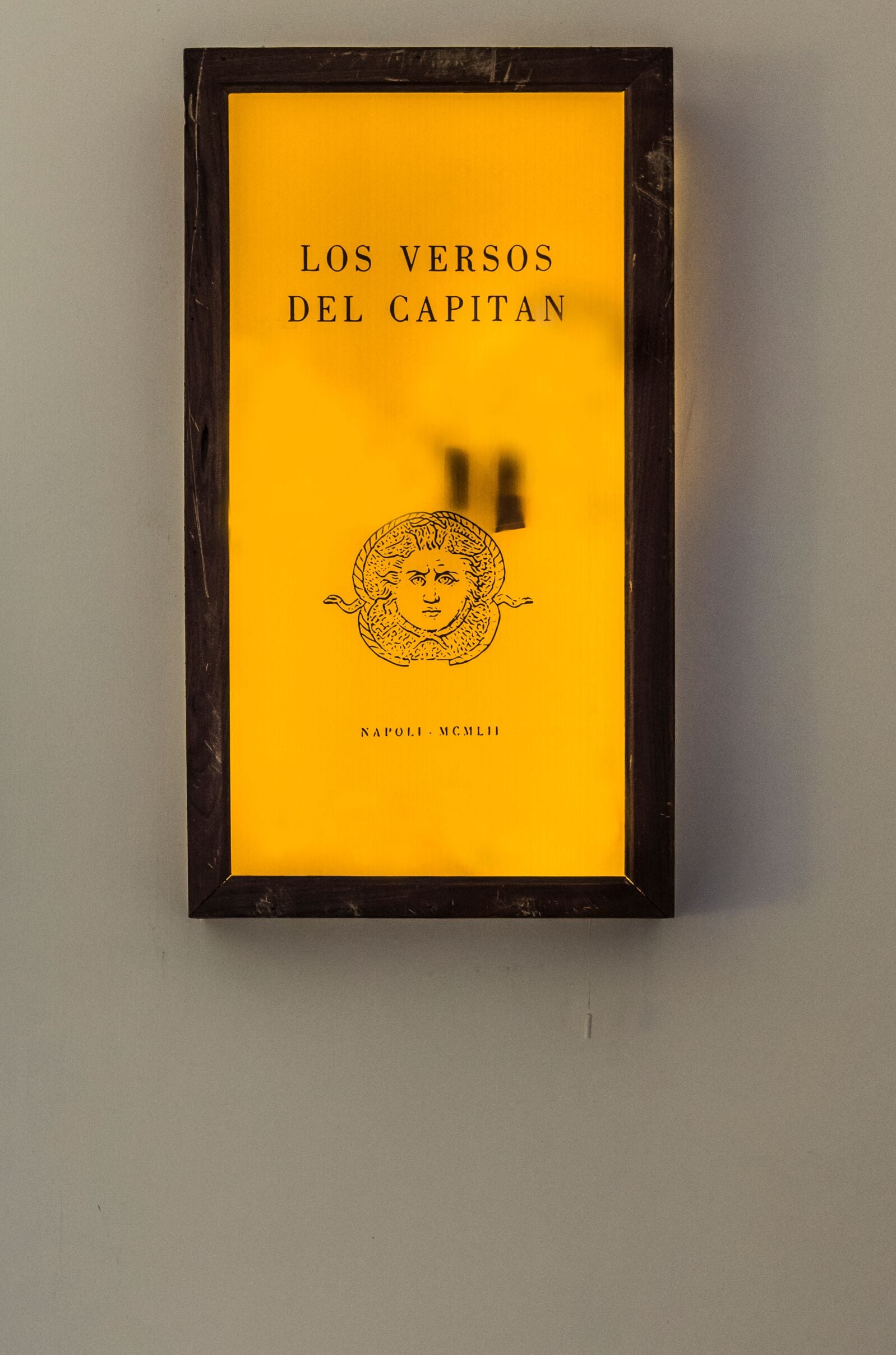 Un libro enmarcado titulado "Los Versos del Capitan", con un borde negro y un fondo amarillo.
