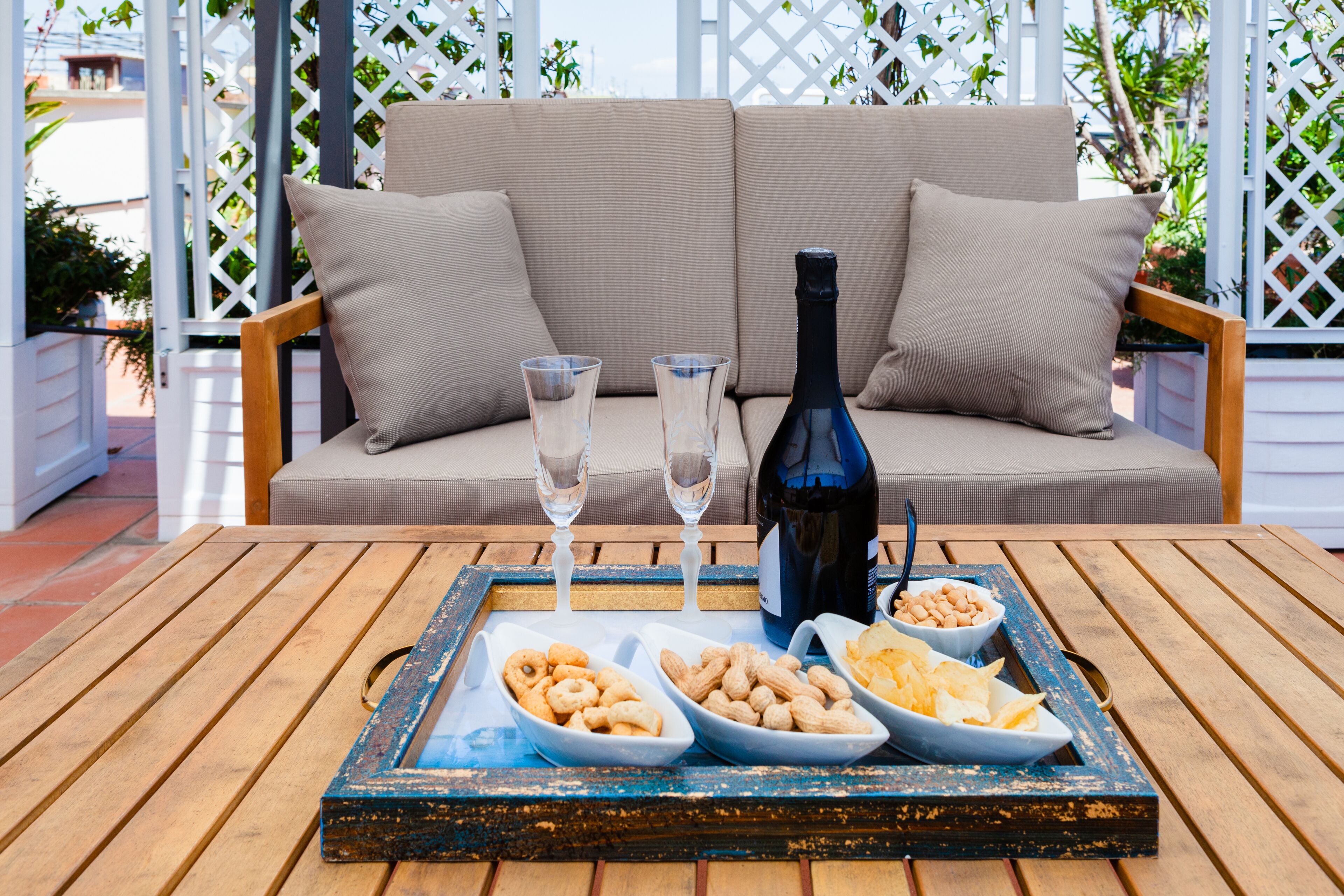 A wooden table with a tray holding snacks, a bottle, and glasses.
