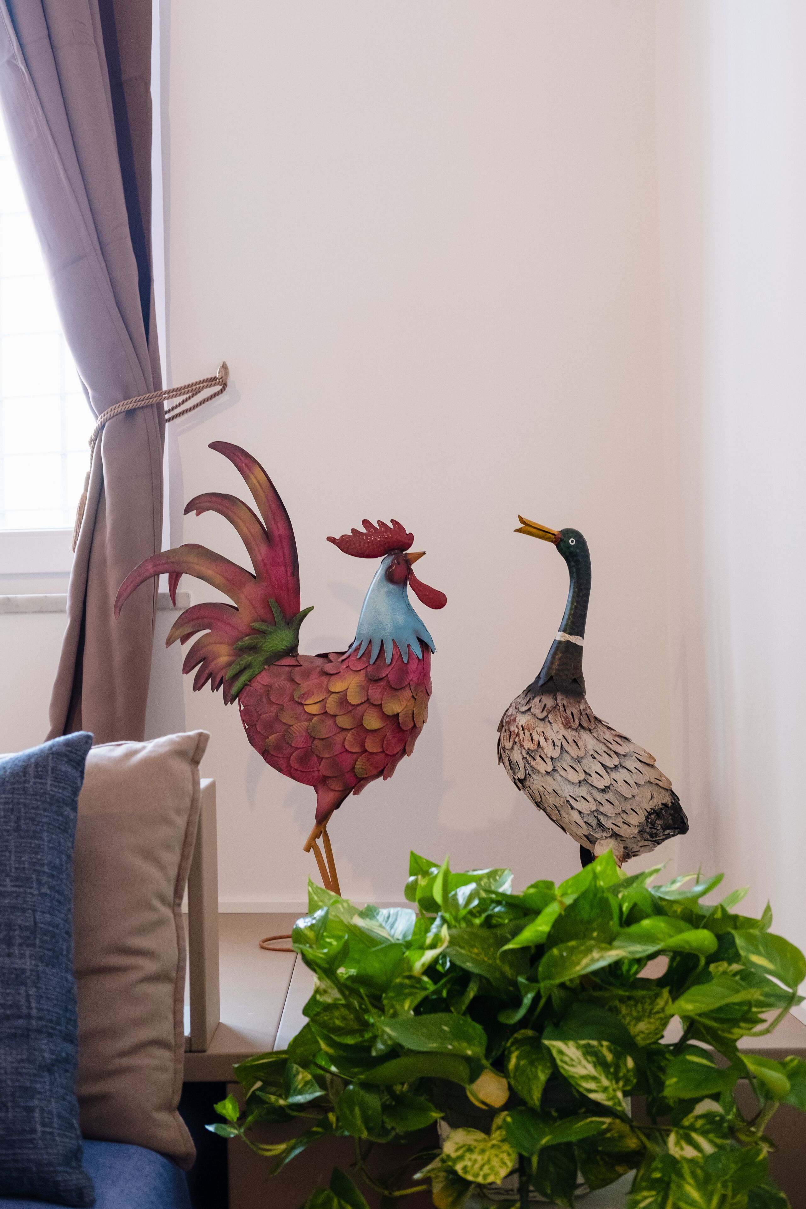A room with a window, a plant, and two wall-mounted decorative birds.