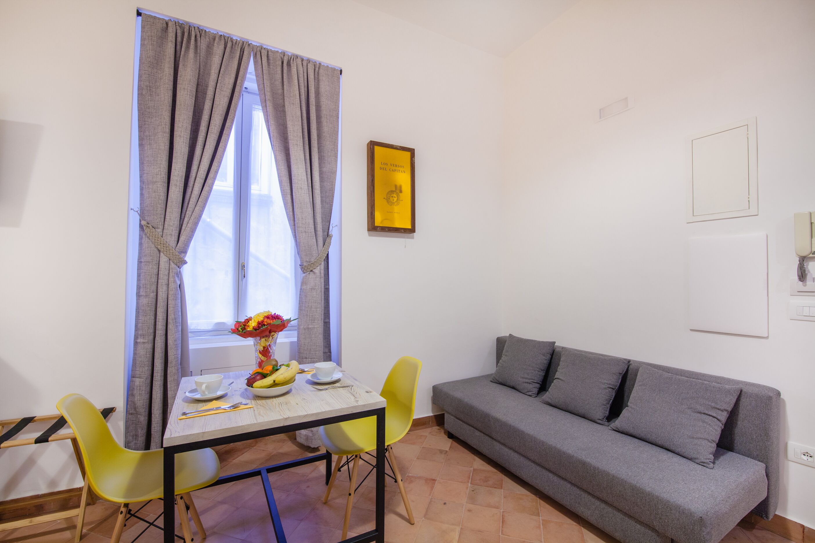 A small living area with a sofa, a table with a vase of flowers, and a window with curtains.