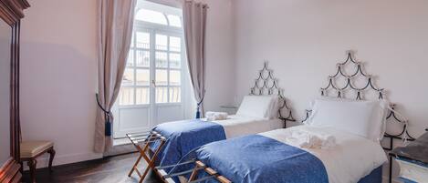 A room with two beds, wooden flooring, a window with curtains, and a wooden ceiling.