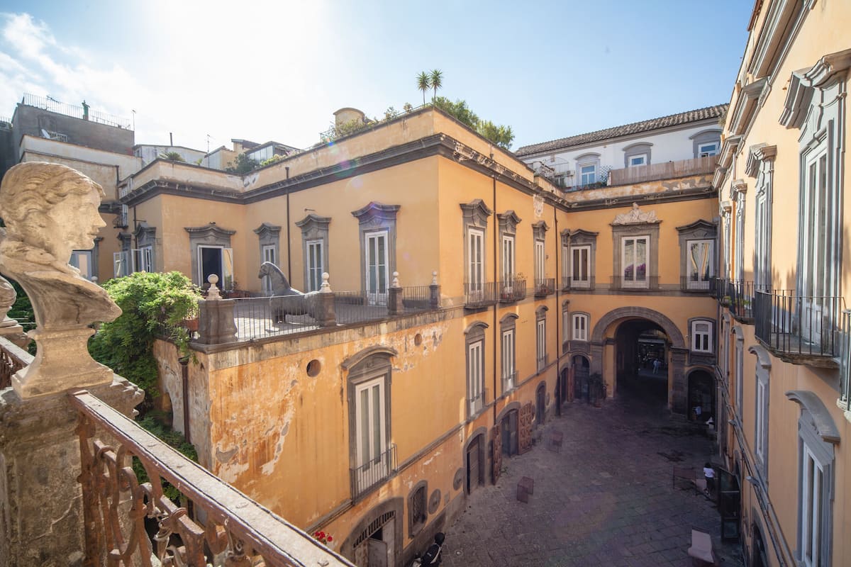 A courtyard with a central archway, surrounded by buildings with balconies and windows.