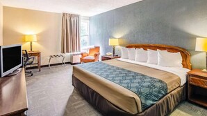 Habitación de hotel con una cama grande, un escritorio con computadora, una silla y dos lámparas de noche.