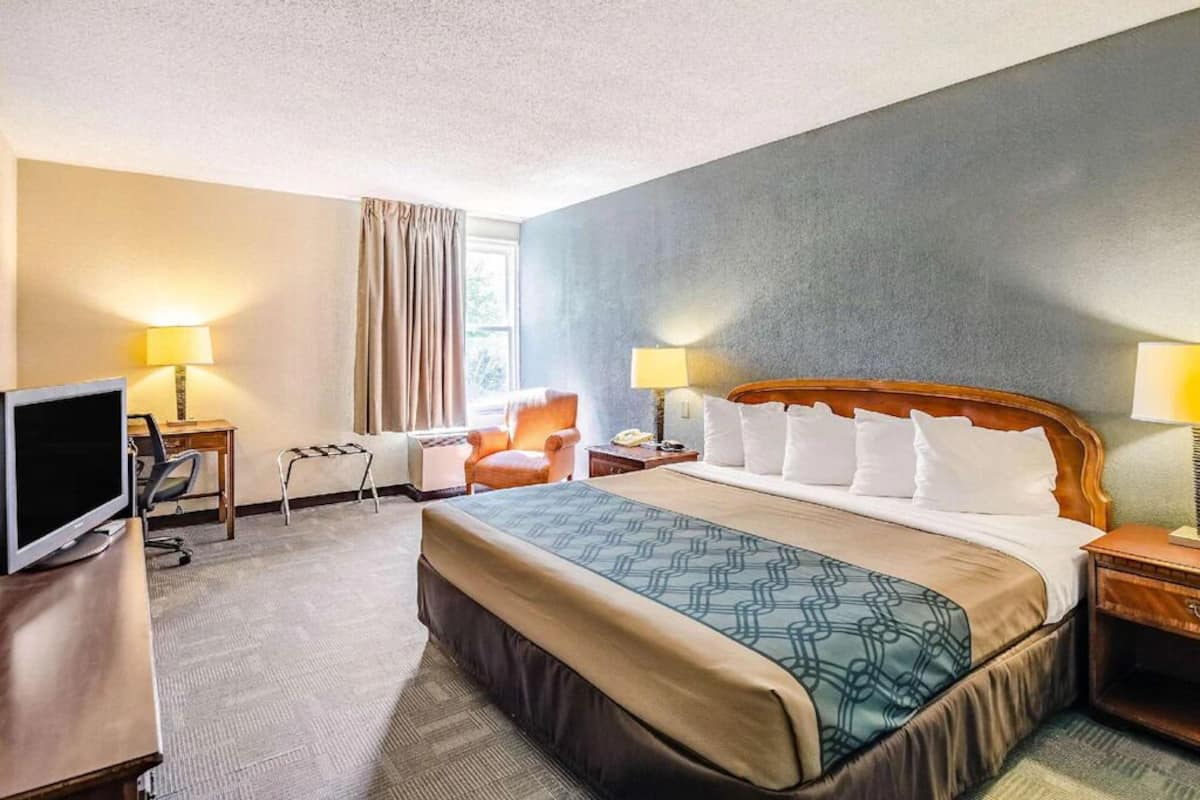 Une chambre d’hôtel avec un grand lit, un bureau avec un ordinateur, une chaise et deux lampes de chevet.