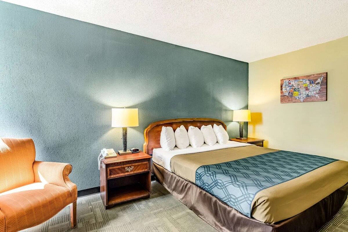 Une chambre d’hôtel avec un lit, deux lampes de chevet, une table de chevet, une chaise et une carte murale.