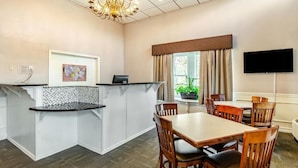 Habitación de hotel con comedor, candelabro, televisor y ventana con cortinas.