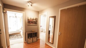 A hallway with wooden flooring, a mirror, a door, and a small shelf with a bowl.