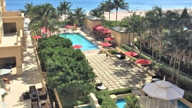 Área de piscina en un resort, con varias piscinas, sillas de descanso y sombrillas, con vista a una playa.