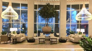 Un vestíbulo con diseño moderno, que presenta un gran árbol central, varias zonas de estar y ventanas amplias con vistas al exterior.