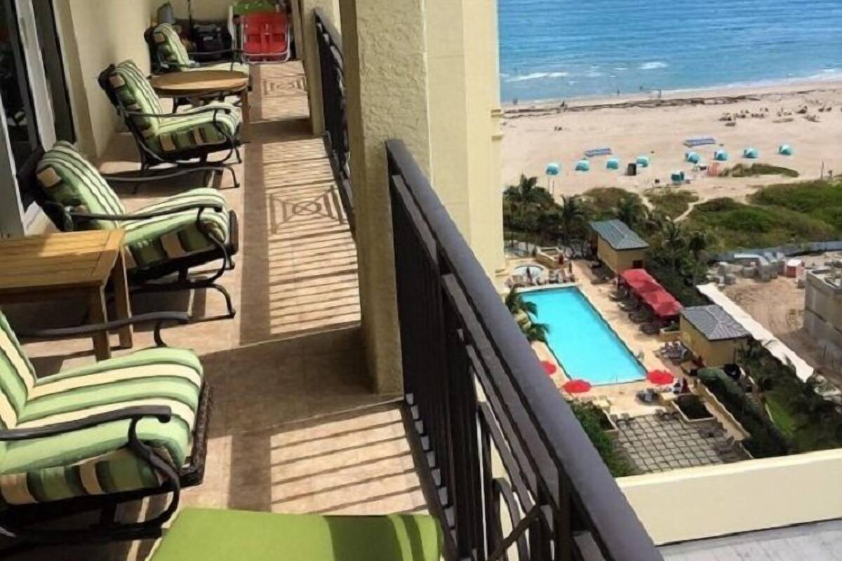 A balcony with green-striped chairs and a pool area with umbrellas.
