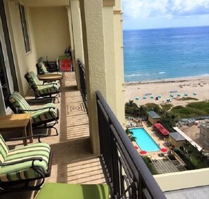 A balcony with green-striped chairs and a pool area with umbrellas. - Condos at Singer Island Resort&Spa (Singer Island)