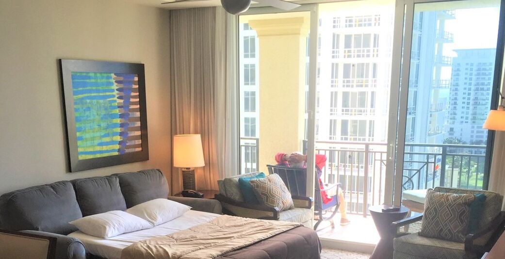 Et hotelværelse med en stor seng, en sofa, en stol, en lampe og udsigt over byen fra vinduet.