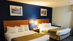 A hotel room with two beds, each with a wooden headboard, white bedding, and a brown throw blanket. There are two framed pictures on the wall, a bedside lamp, and a nightstand with a clock. - Hotel Northern Star (Slave Lake)