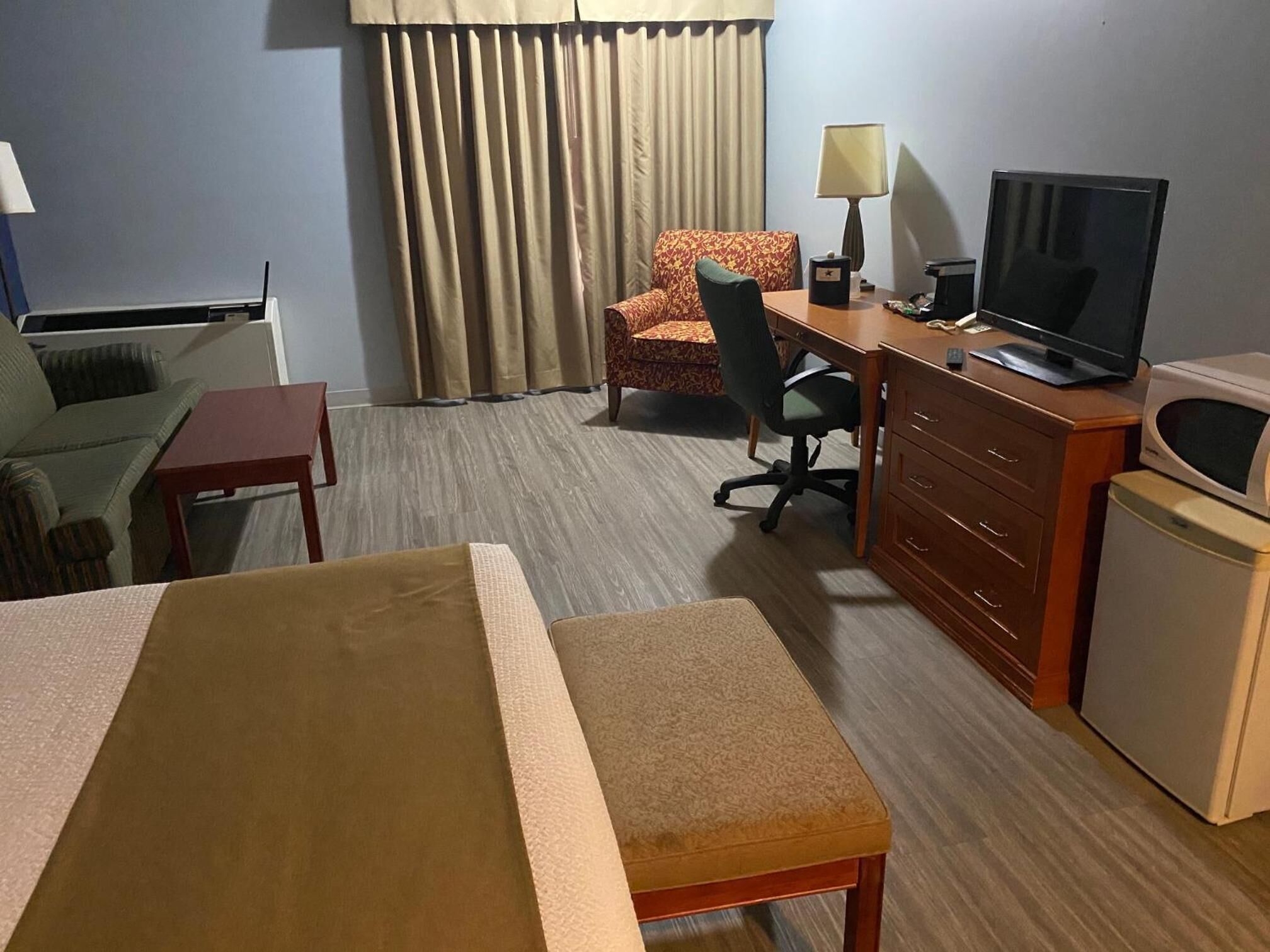 A hotel room with a bed, a desk with a computer, a television, a chair, a lamp, and a small refrigerator.