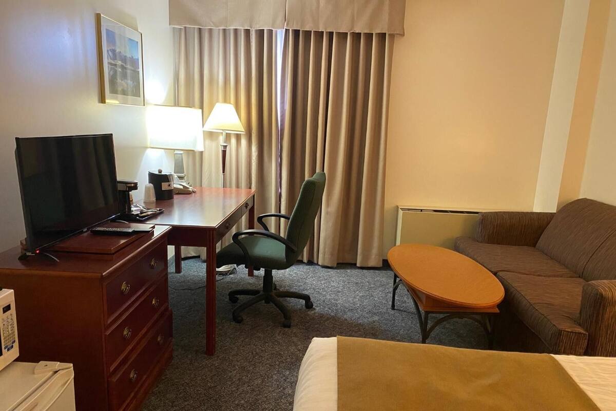 A hotel room with a bed, a desk with a computer, a chair, a sofa, and a TV.