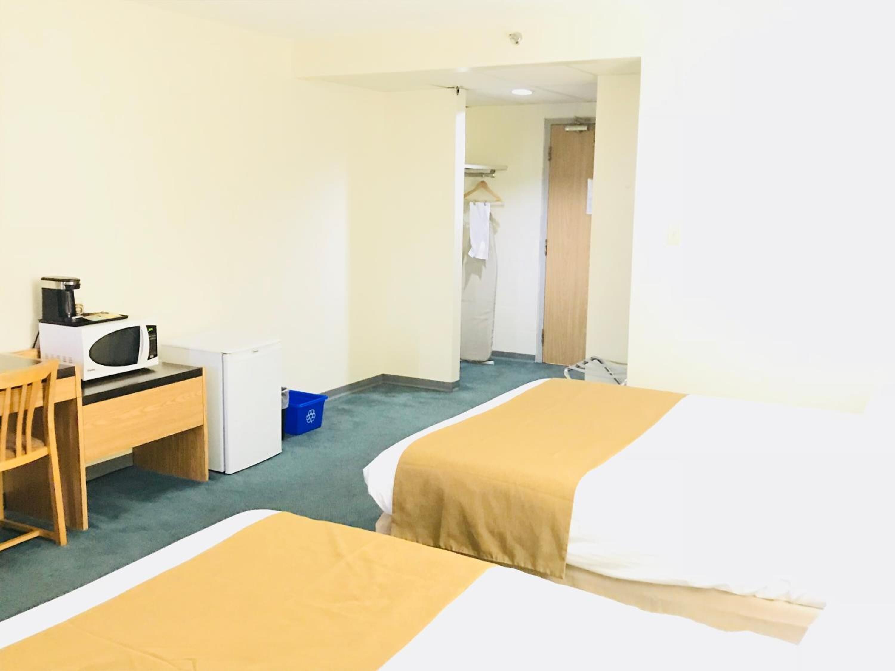 A hotel room with two beds, a desk with a microwave, a chair, and a blue trash bin.