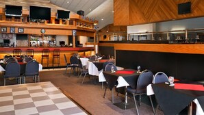 A restaurant with multiple tables and chairs, a bar area with shelves of bottles, and a large screen on the wall. - Hotel Northern Star (Slave Lake)