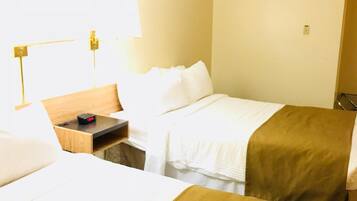 A hotel room with two beds, a bedside table with a clock, a lamp, and a window with curtains.