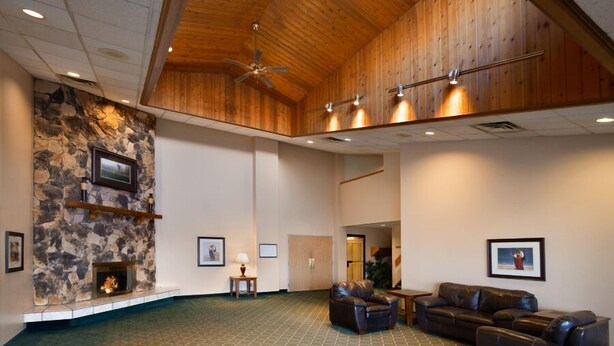 A spacious lobby with a stone fireplace, leather sofas, and a high ceiling with wooden beams. - Hotel Northern Star (Slave Lake)